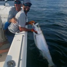 Two men holding a large fish off the side of a boat